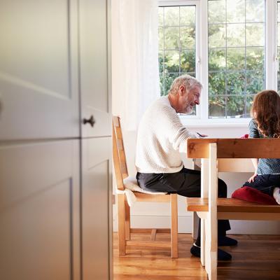 A grandfather and his granddaughter in the dining room doing a coloring activity together.