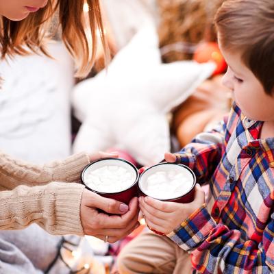 A young boy holding a cup of hot chocolate with his mother.