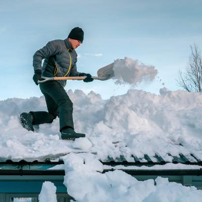Young person shoveling heavy snow on a rooftop.