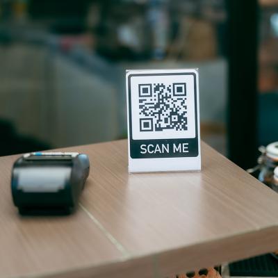 A 'scan me' QR code sign and payment terminal on a cafe reception table.
