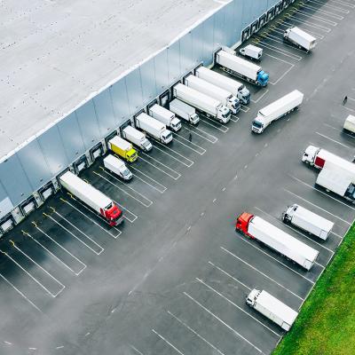 Aerial view of logistic trucks lined up at the loading docks of a large distribution warehouse.