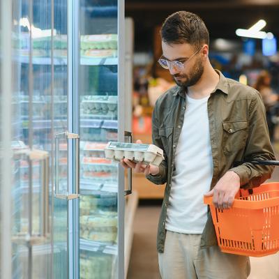 A young man checking eggs from a grocery store shelf.