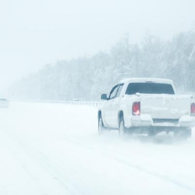 Rear view of a white pickup truck on the road during heavy snowfall.
