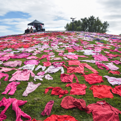 The XR Guerrilla Fashion's protest in Utrecht's Griftpark showcased a 7,000-garment installation by Pet van de Luijtgaarden. Red and pink clothing is laid out on a grassy field with a small tent of a few people in the distance.