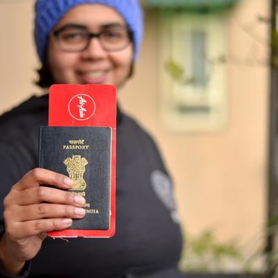 Portrait of a young Indian woman holding up her passport with an international flight ticket.