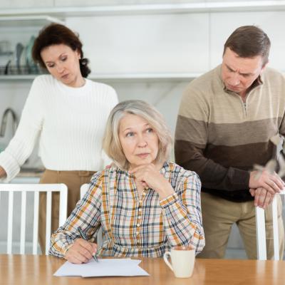 A senior woman signing documents with adult children behind her.