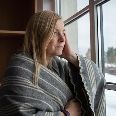 Woman wrapped in blanket looking out the window during winter.