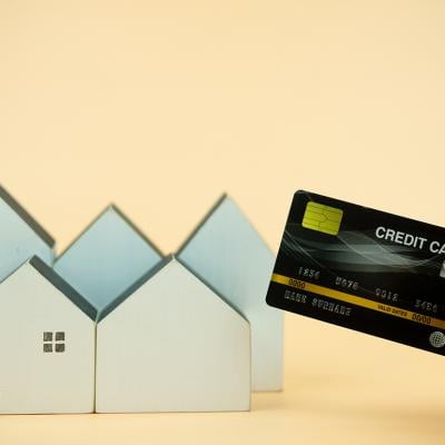Hand holding a credit card over small figures of houses.