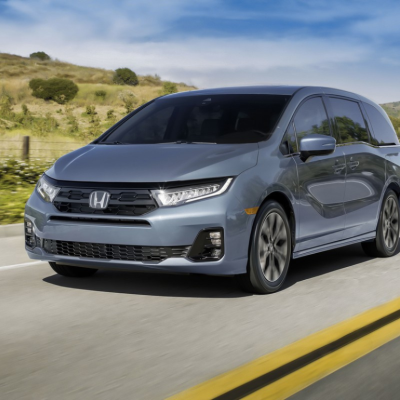 A dark gray Honda Odyssey driving down a rural road. 