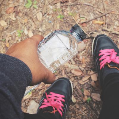 A selfie-style photo showing a person holding a water bottle and their fitness shoes while outdoors.