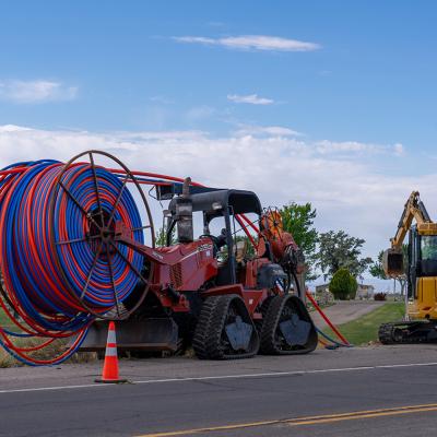 Machinery vehicles parked on roadside while installing internet fiber optic cables' plastic conduit underground in a rural area in Utah.