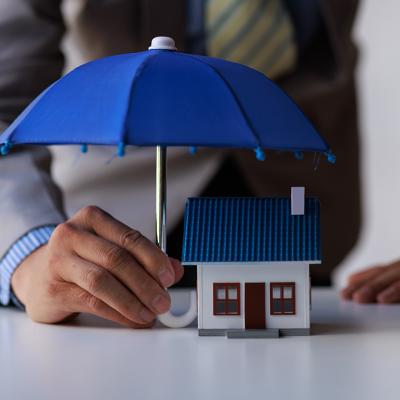 A figure of a house with a person holding small umbrella over it as a concept of home insurance.