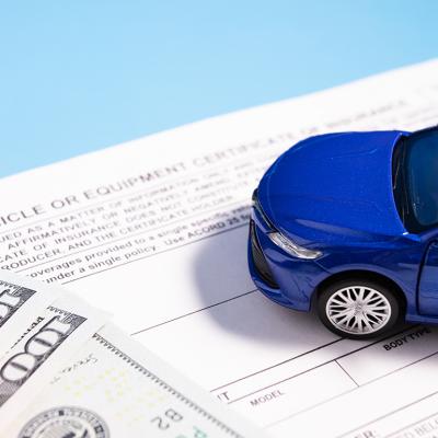 A small figure of a blue car on top of banknotes and insurance documents.
