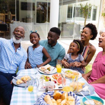 An older man smiling while taking selfie with his family at an outdoor dining table during brunch. 
