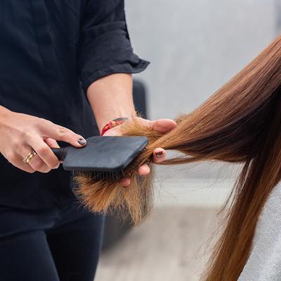 A professional hairstylist combing a client's hair with a paddle hairbrush.