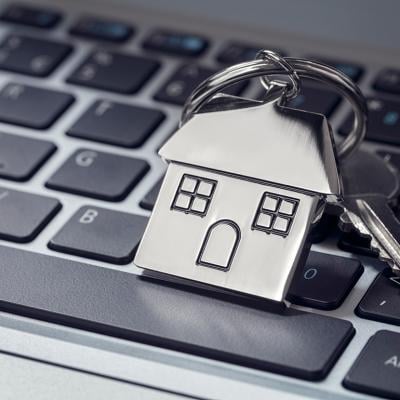 A house key and steel house keychain on top of a laptop keyboard.