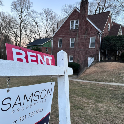 A sign in foreground lists a home for rent in Maryland with tall brick home in the background. Municipal rental registries are gaining attention as cities try to get a handle on who owns rental properties and where, both to better understand their housing landscape and to ensure rentals are safe for tenants. 