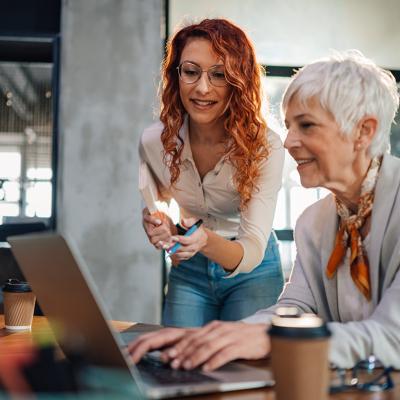 A senior employee working with a younger colleague on a task in an office.