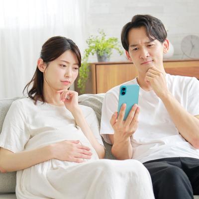 A pregnant wife and her husband curiously browsing information on a smartphone while sitting on a sofa at home.