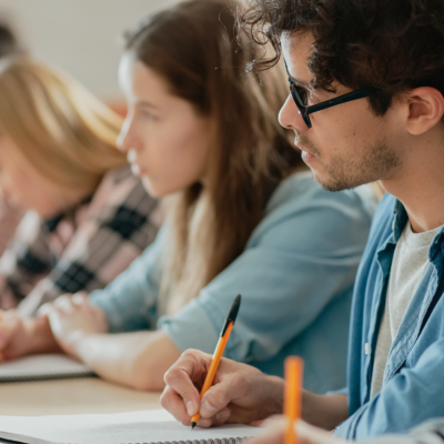 Teenage or young adult students seated in a row, taking notes. 