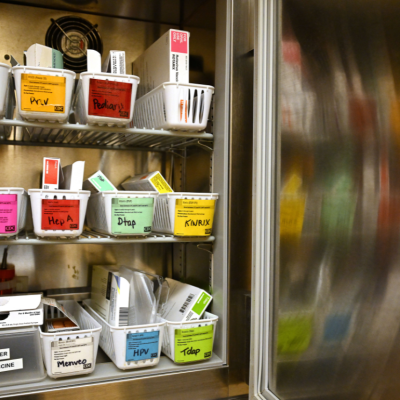 A small open refrigerator with shelves of baskets of vaccines at a health clinic.