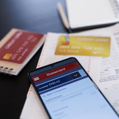 A close up on a credit card statement opened from a phone on top of physical credit cards and receipts.