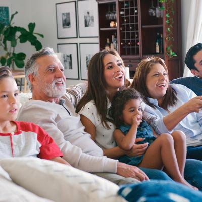 A multi-generational family sitting together on a sofa and watching televisions.