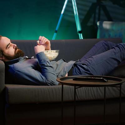 A bored man lying on couch and eating popcorn.