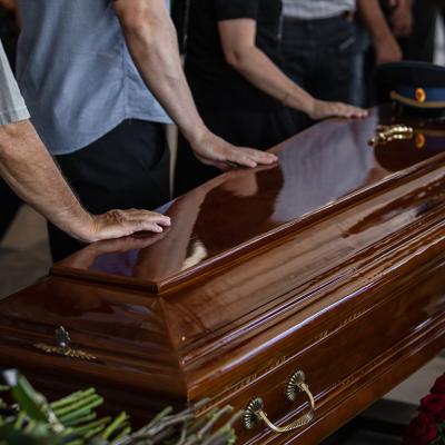 People touching the wooden brown coffin of a deceased relative.