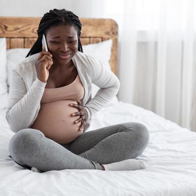 A pregnant young black woman calling on the phone while experiencing pain in her belly.