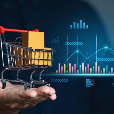 Concept of retail sales illustrated by perosn holding miniature shopping cart with packages inside; chart with growth figures and data in the background 