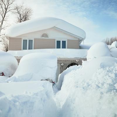 A house and its cars covered in deep white snow after a blizzard.