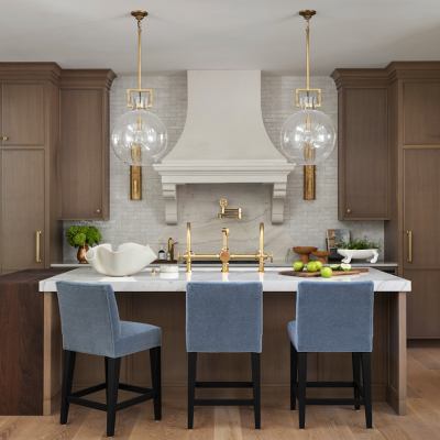 A kitchen with wooden cabinets, modern gold fixtures and light blue velvet chairs around a center island.