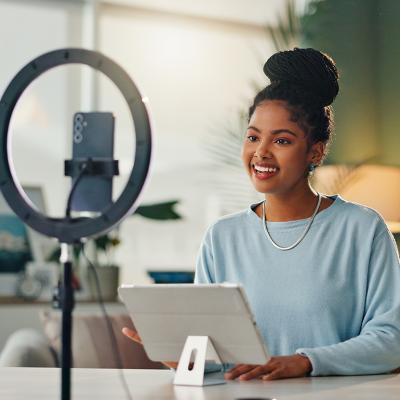 A young woman filming vlog content at home using her smartphone and a tripod.