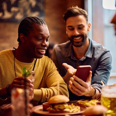 Happy men looking on their phones while sitting in a bar.