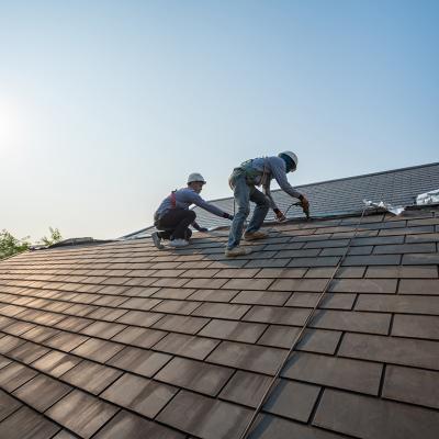 Two roof workers in full gear as they replace tiling on a roof.