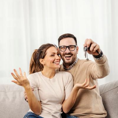 A happy couple taking a photo and showing off their new home's keys to the camera.
