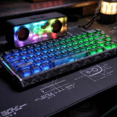 A blue-lit mechanical keyboard and a rainbow-colored speaker on a desk.