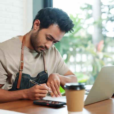 A young small cafe business owner reviewing reports at a cafe desk.
