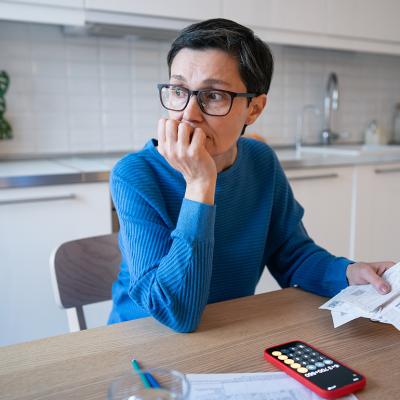 A stressed middle-aged woman looking away from bills at home.
