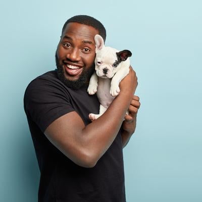 A young black man happily posing with his french bulldog puppy.