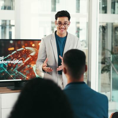 A young male public speaker giving a talk about digital transformation to a group of corporate employees at a conference.