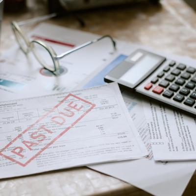 Bills stamped with a past due sign beside a calculator on top of a desk.