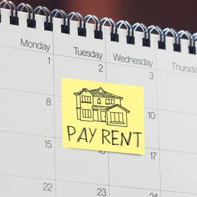 A note written with 'pay rent' as a reminder stuck onto a calendar.