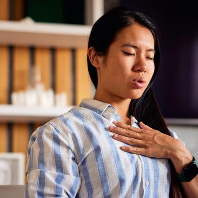 A young woman with her hand on her chest, practicing a breathing technique at home.
