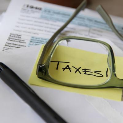 A low-angle view of tax documents and the word 'Taxes' written on a yellow sticky note viewed through eyeglasses.