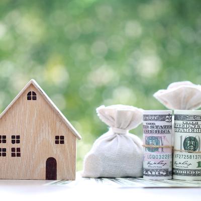 A wooden figure of a model house with banknotes on the side as a concept of saving money for a home.