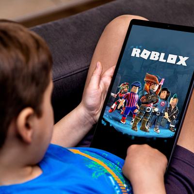 A young child sitting on a sofa and playing Roblox using a tablet.