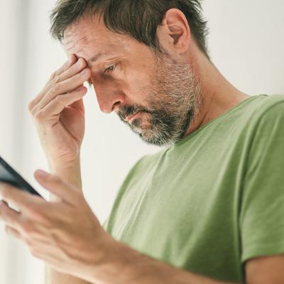 Man at home reading a worrying text message.