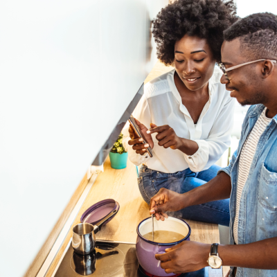 Young couple is using a smartphone and smiling while cooking in kitchen at home.